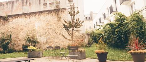 An outdoor patio with a stone wall, a small tree, potted plants, and outdoor furniture.