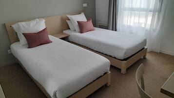 A hotel room with two single beds, each with white bedding and a wooden headboard.