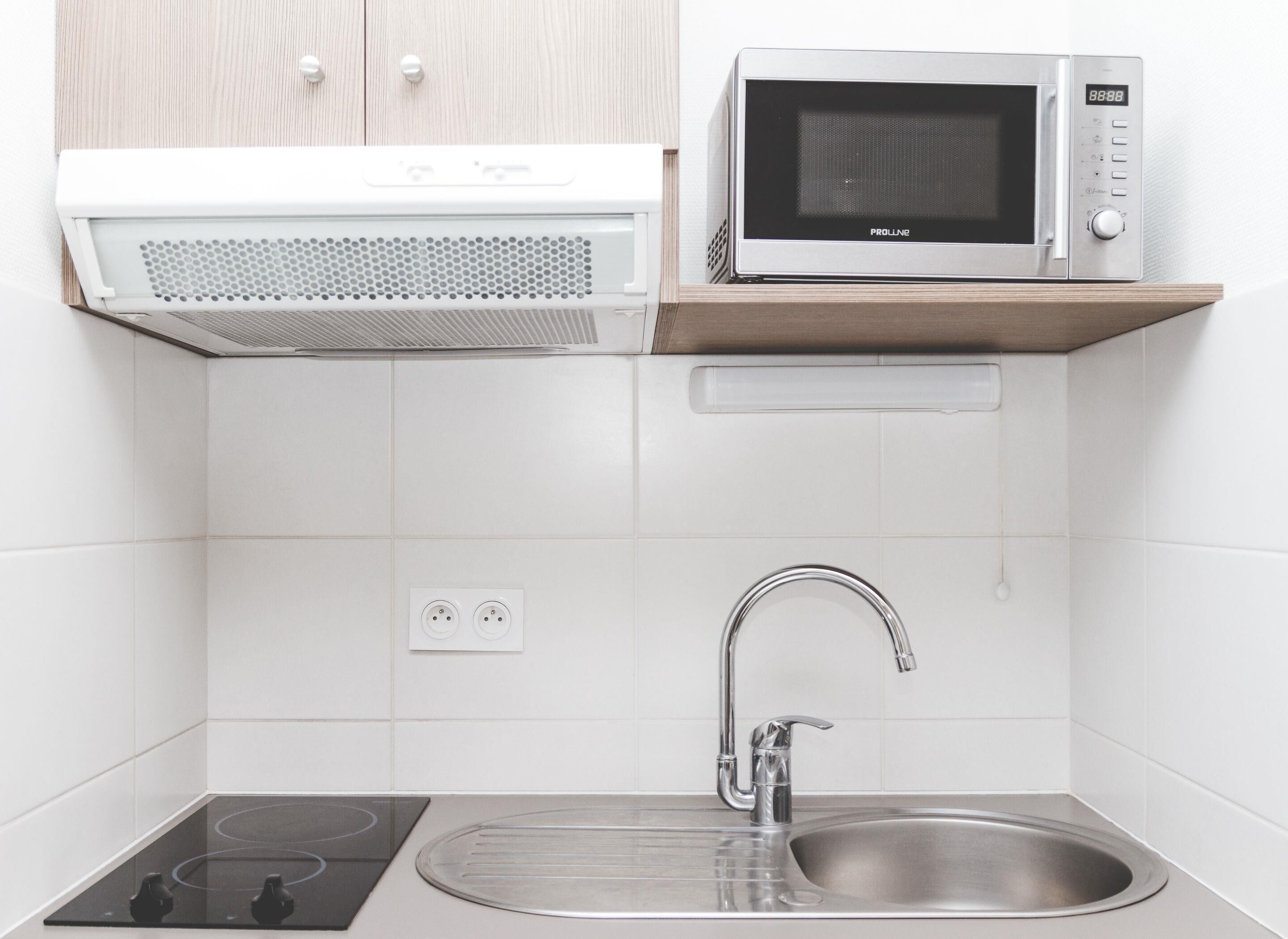 A kitchen with a microwave, stove, sink, and wooden cabinet.