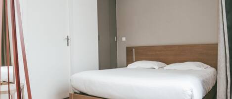 Un dormitorio con estructura de cama de madera, ropa de cama blanca y una puerta con manija.