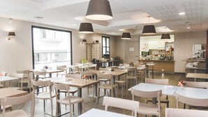 Un'ampia sala da pranzo con diversi tavoli e sedie, ampie finestre e lampade a sospensione.