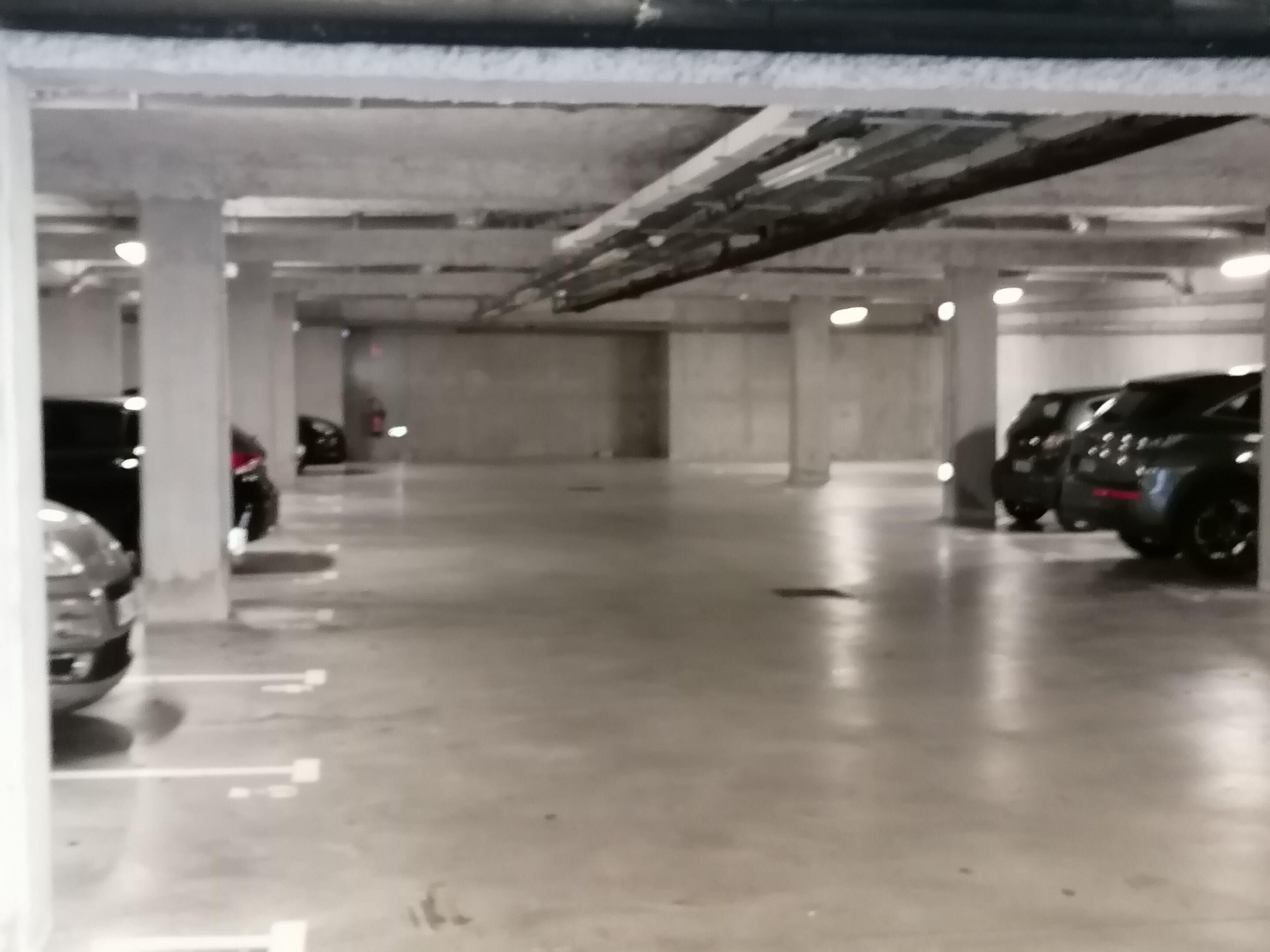 Un estacionamiento de varios niveles con pilares de hormigón y algunos coches aparcados.