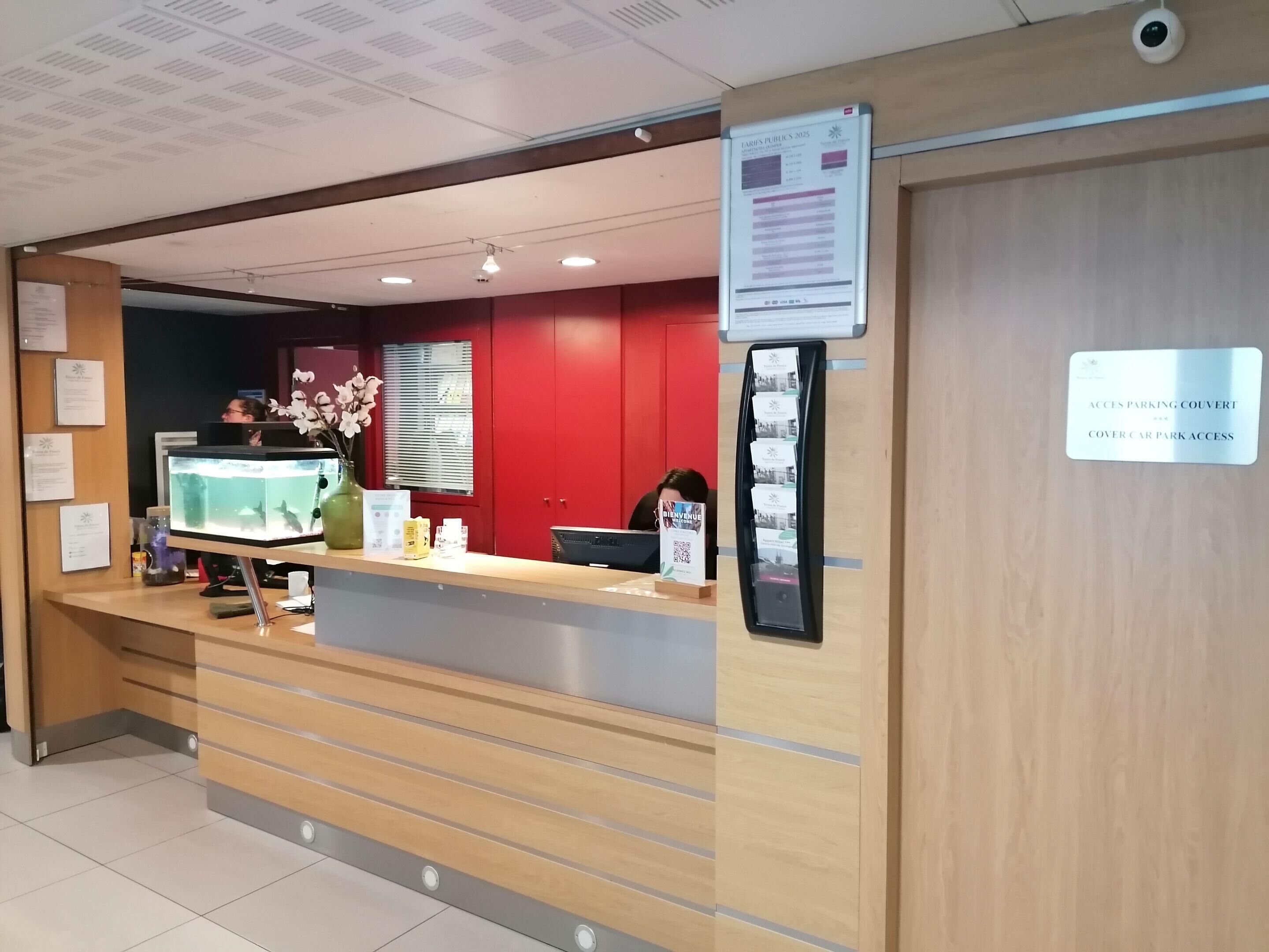 A reception desk with a computer monitor, a vase with flowers, and a sign indicating access to parking.