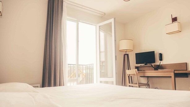 Camera d'albergo con un letto, una scrivania, una sedia, un computer, una lampada e vista sull'esterno.