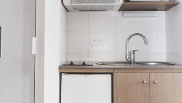 Una cocina compacta con armarios de madera, microondas integrado, un lavamanos y un refrigerador pequeño.