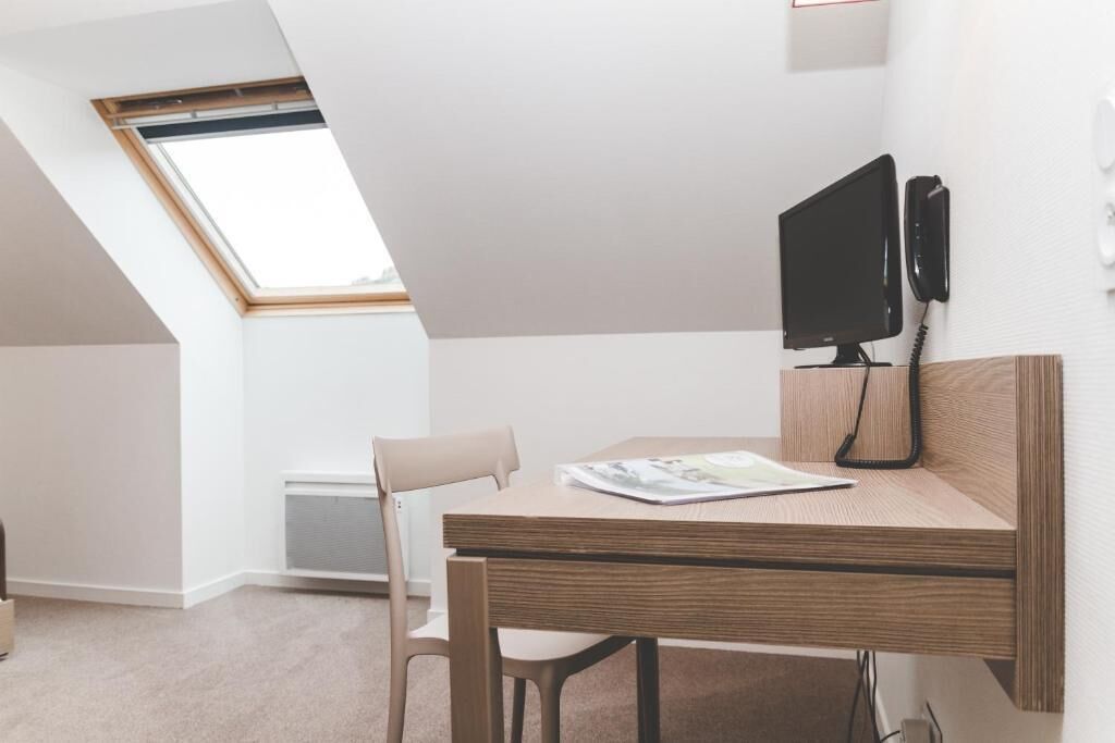 A modern, minimalistic room with a sloped ceiling, a desk with a computer monitor, and a chair.