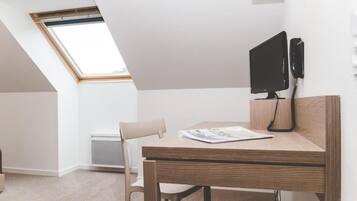 Una habitación moderna y minimalista con techo inclinado, un escritorio con monitor de computadora y una silla.