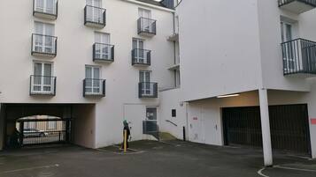 Un edifici residencial de diversos pisos amb balcons, una entrada tancada amb reixa i una zona d'aparcament.