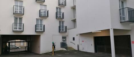 A multi-story residential building with balconies, a gated entrance, and a parking area.