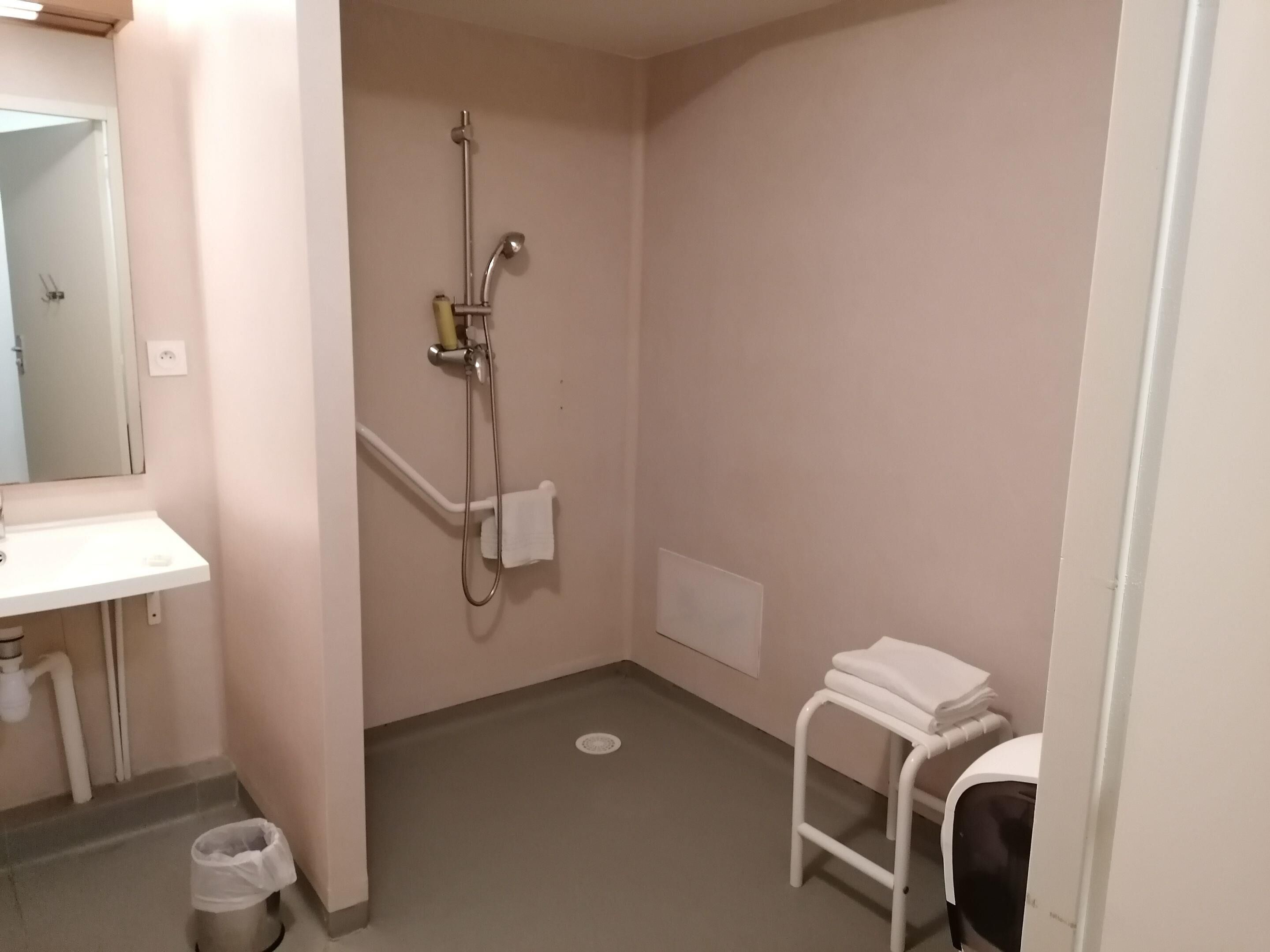 A small bathroom with a sink, a shower, a toilet, and a trash bin.
