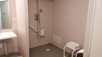 A small bathroom with a sink, a shower, a toilet, and a trash bin.