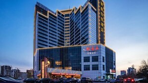 A modern hotel with a prominent glass facade, multiple floors, and a parking lot in front. - Inzone Garland Hotel Jinan (Jinan)