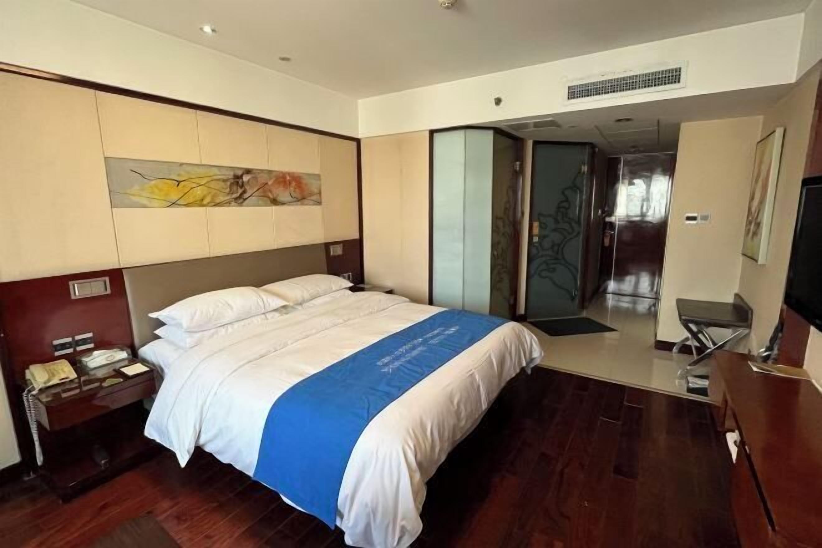 A hotel room with a bed, a desk with a telephone, a television, and a sliding door leading to another room.