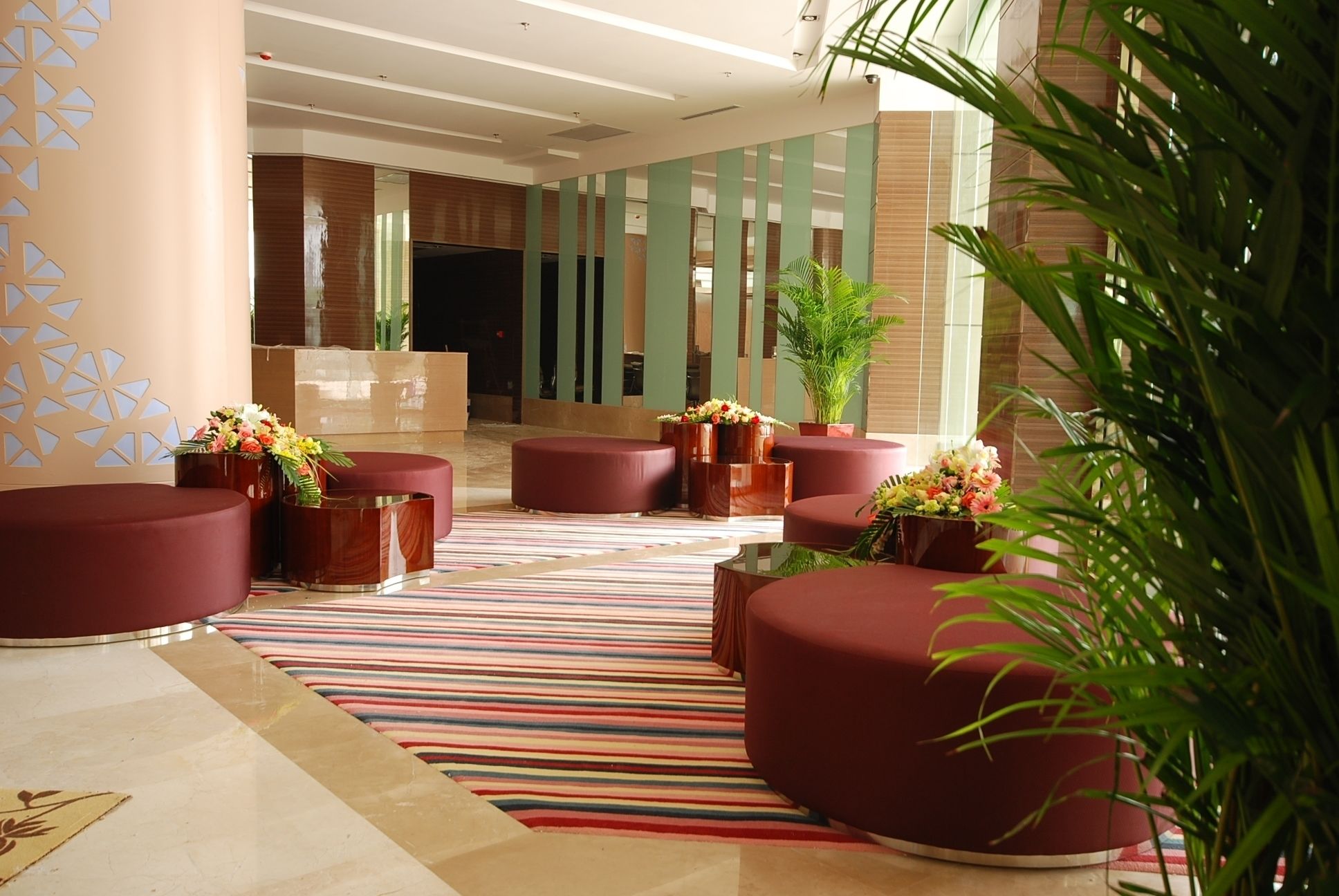 A modern lobby with red seating, striped carpet, and potted plants.