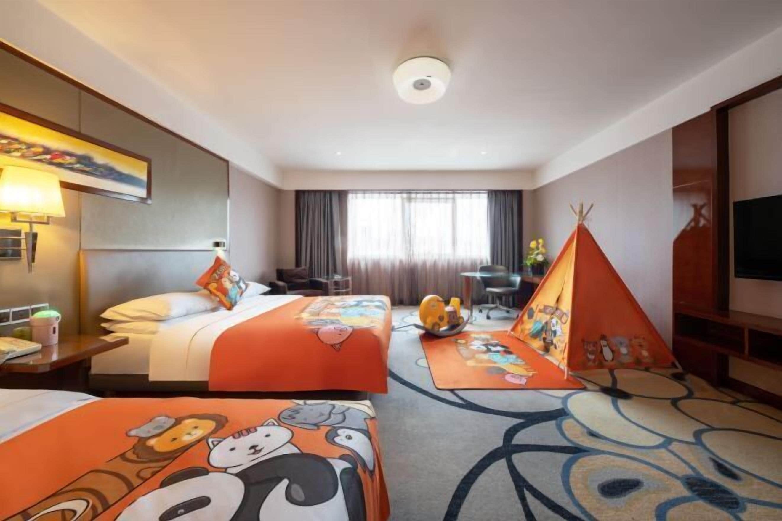 A hotel room with two beds, a large window, a TV, and a children's play area.