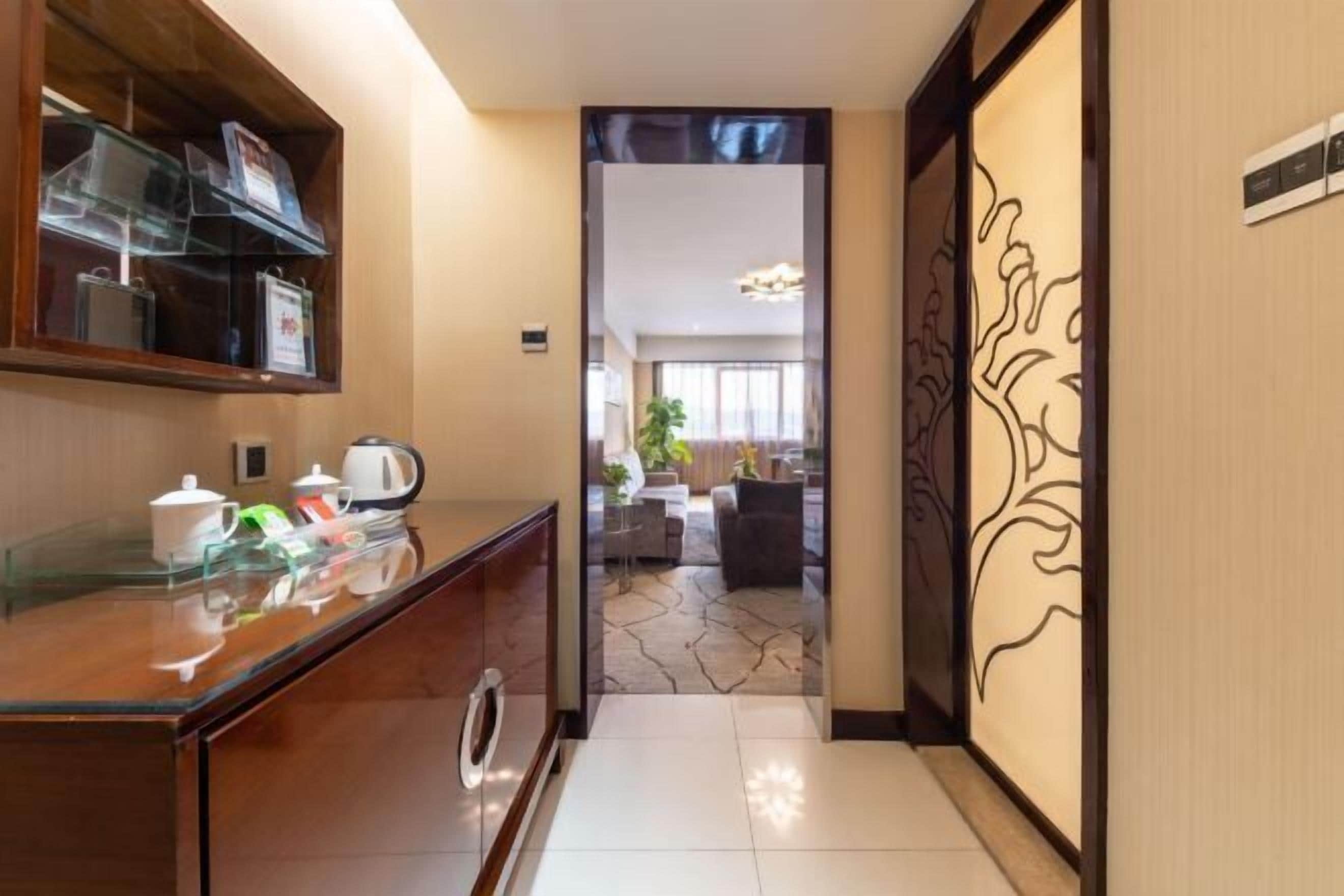 A hotel lobby with a reception desk, a coffee station, and a view into a living area with a sofa and a plant.