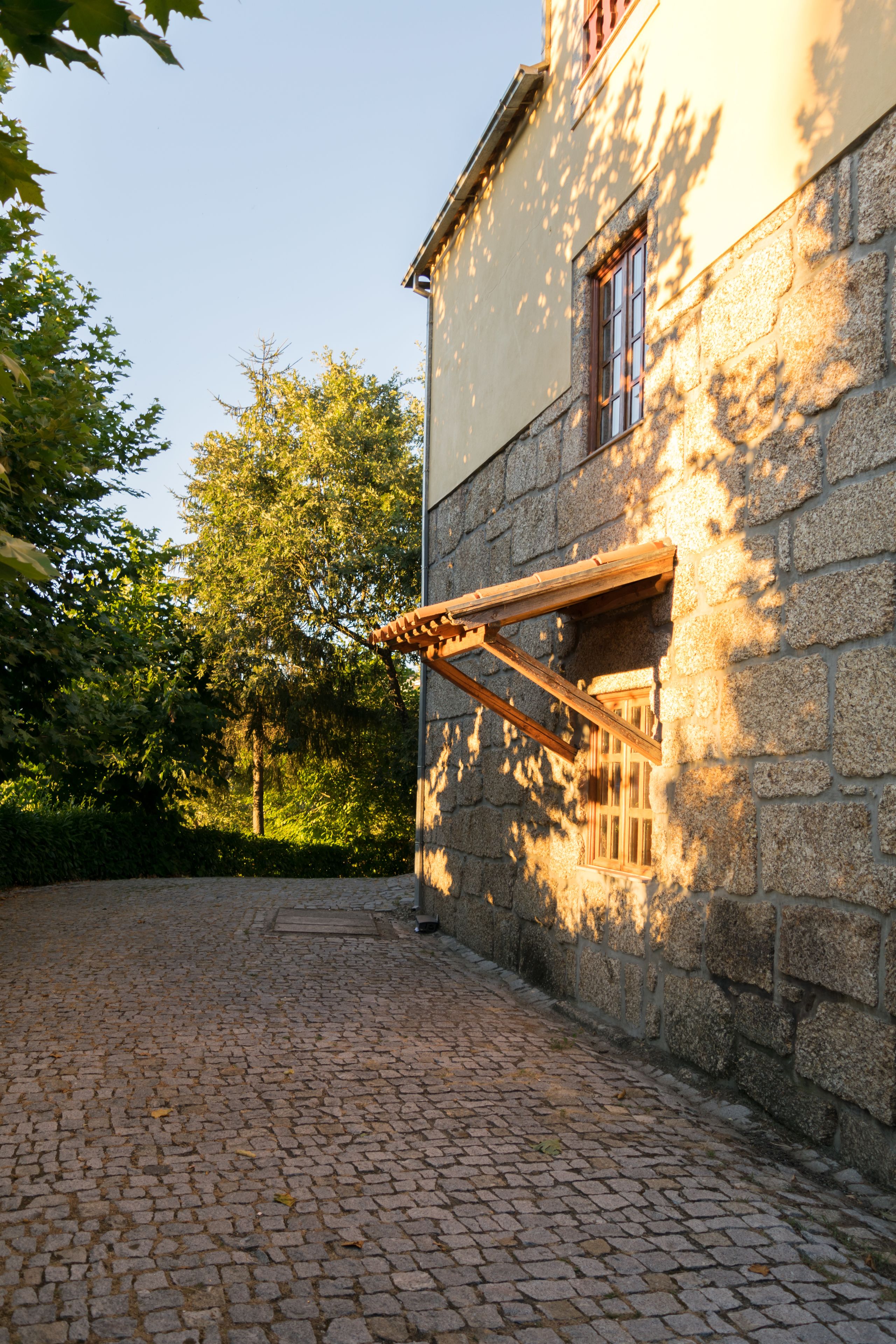 A cobblestone courtyard with a stone building featuring a wooden window frame and a wooden awning.