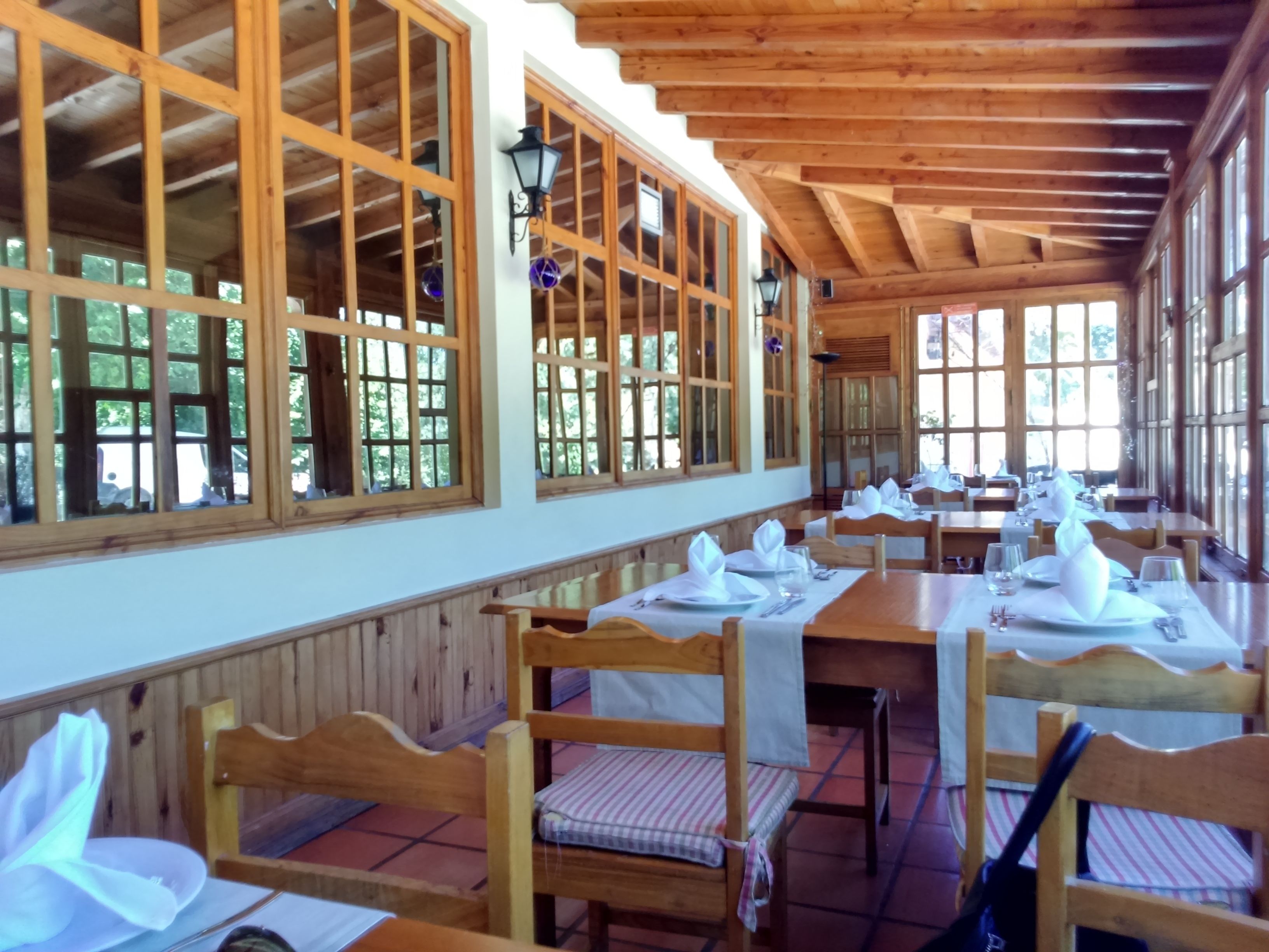 Ein Restaurant mit Holztischen und -bänken, großen Fenstern und einer hohen Decke.