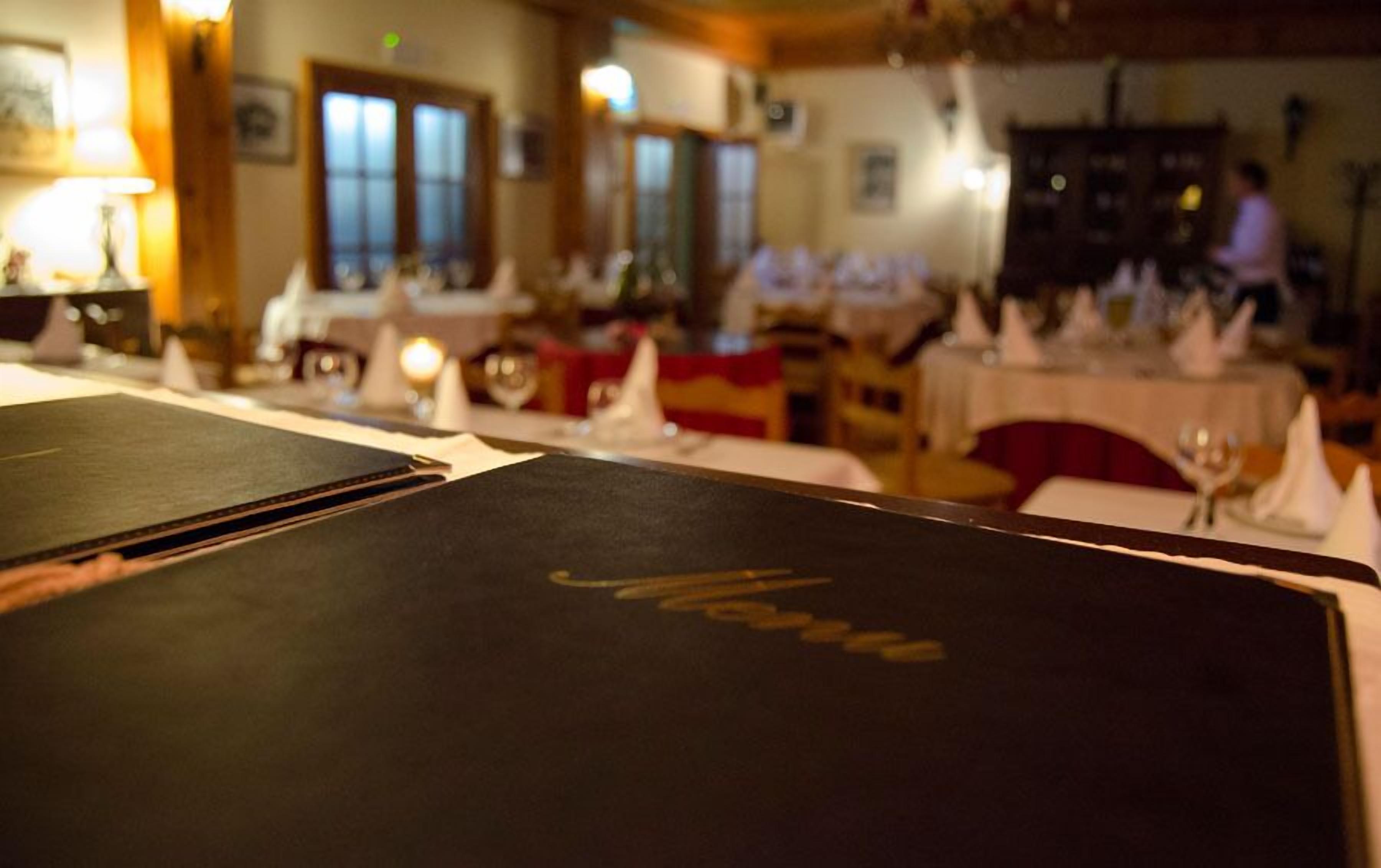 A restaurant interior with tables set for dining, a menu stand, and a person in the background.