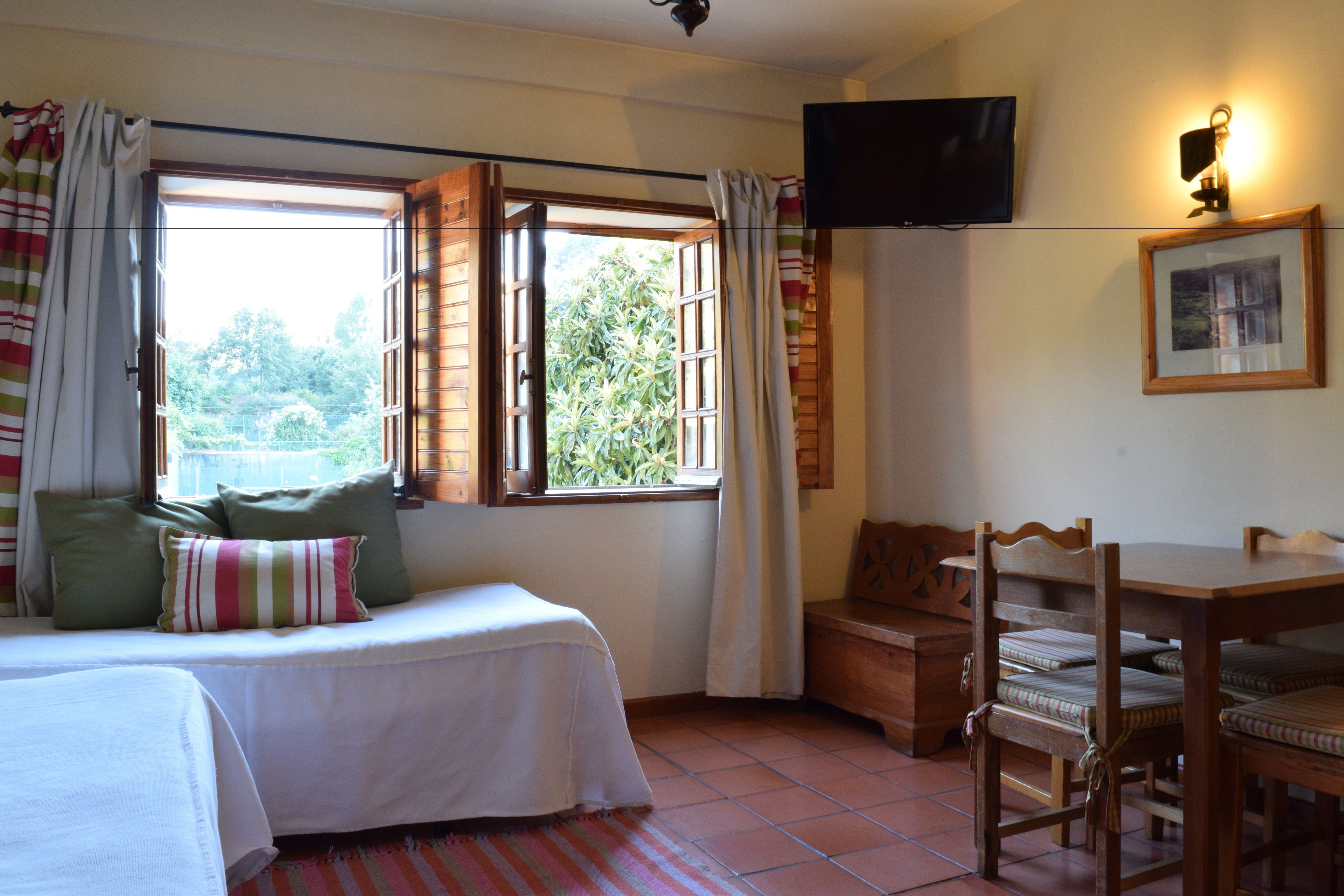 A bedroom with a bed, a wooden bench, a table, and a TV mounted on the wall.
