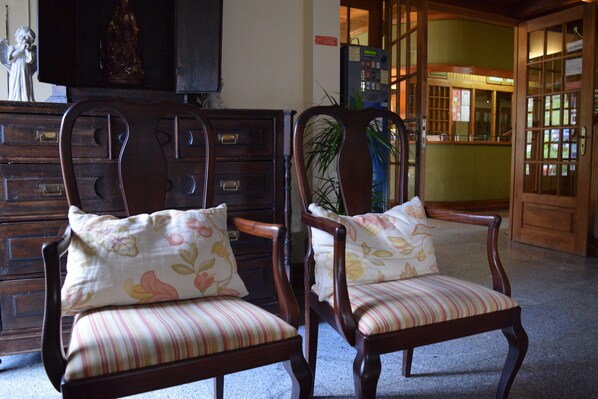 Dos sillas de madera con tapicería a rayas y almohadones florales, ubicadas en un vestíbulo con un aparador de madera y una estatua a la izquierda.