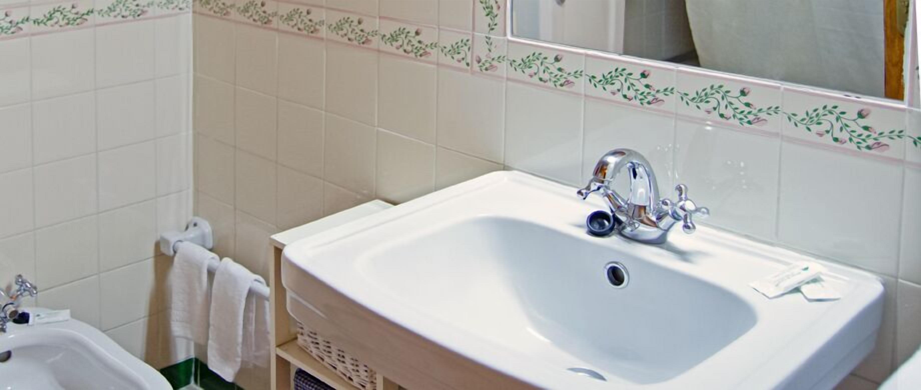 Un baño con lavamanos blanco, un espejo y un perchero para toallas.