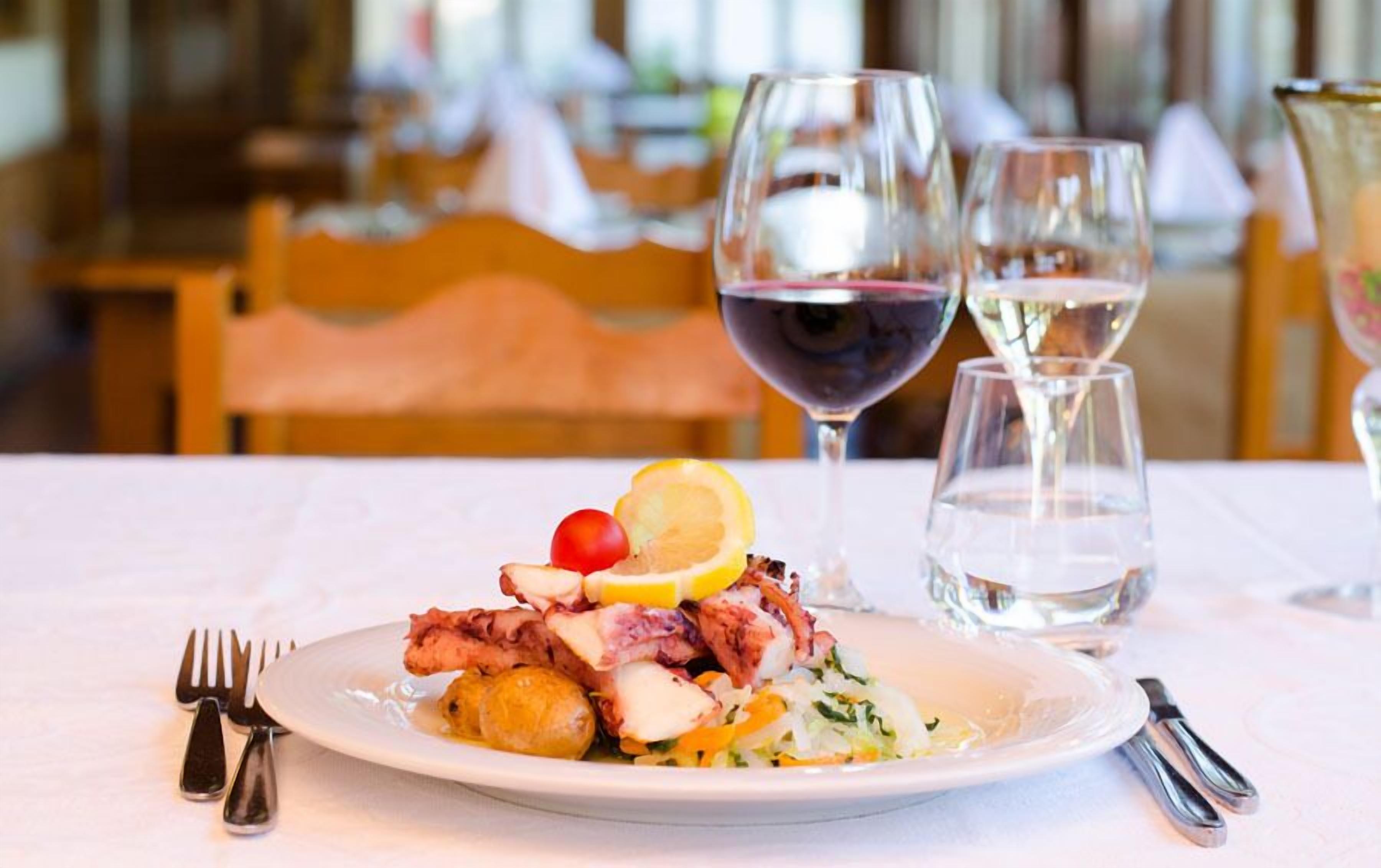 A plate of food with a lemon slice, cherry, and a salad, accompanied by two glasses of wine and a glass of water on a table.