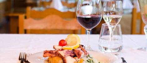 A plate of food with a lemon slice, cherry, and a salad, accompanied by two glasses of wine and a glass of water on a table.