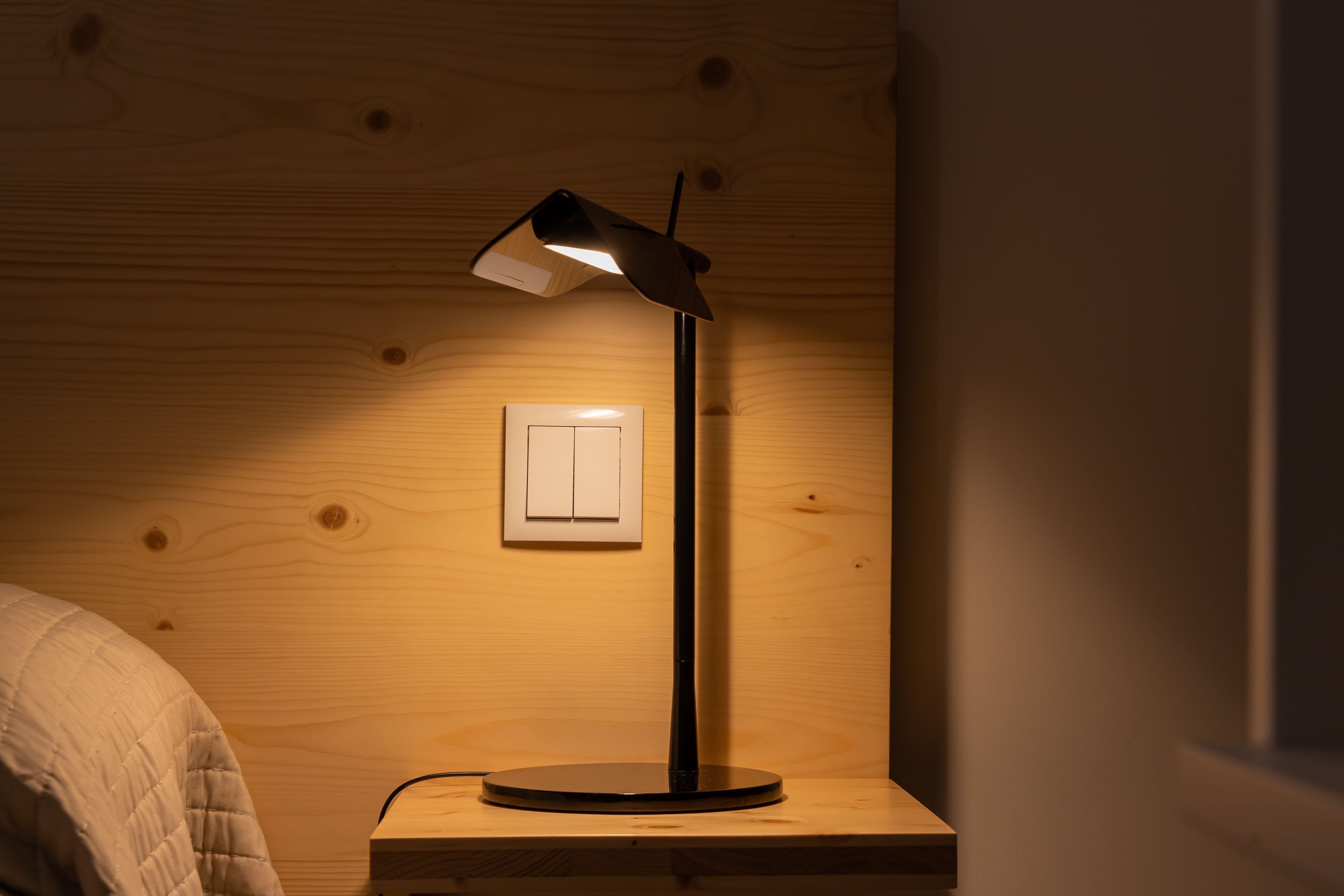 Eine Holzwand mit einem weißen Lichtschalter und einer schwarzen Schreibtischlampe.