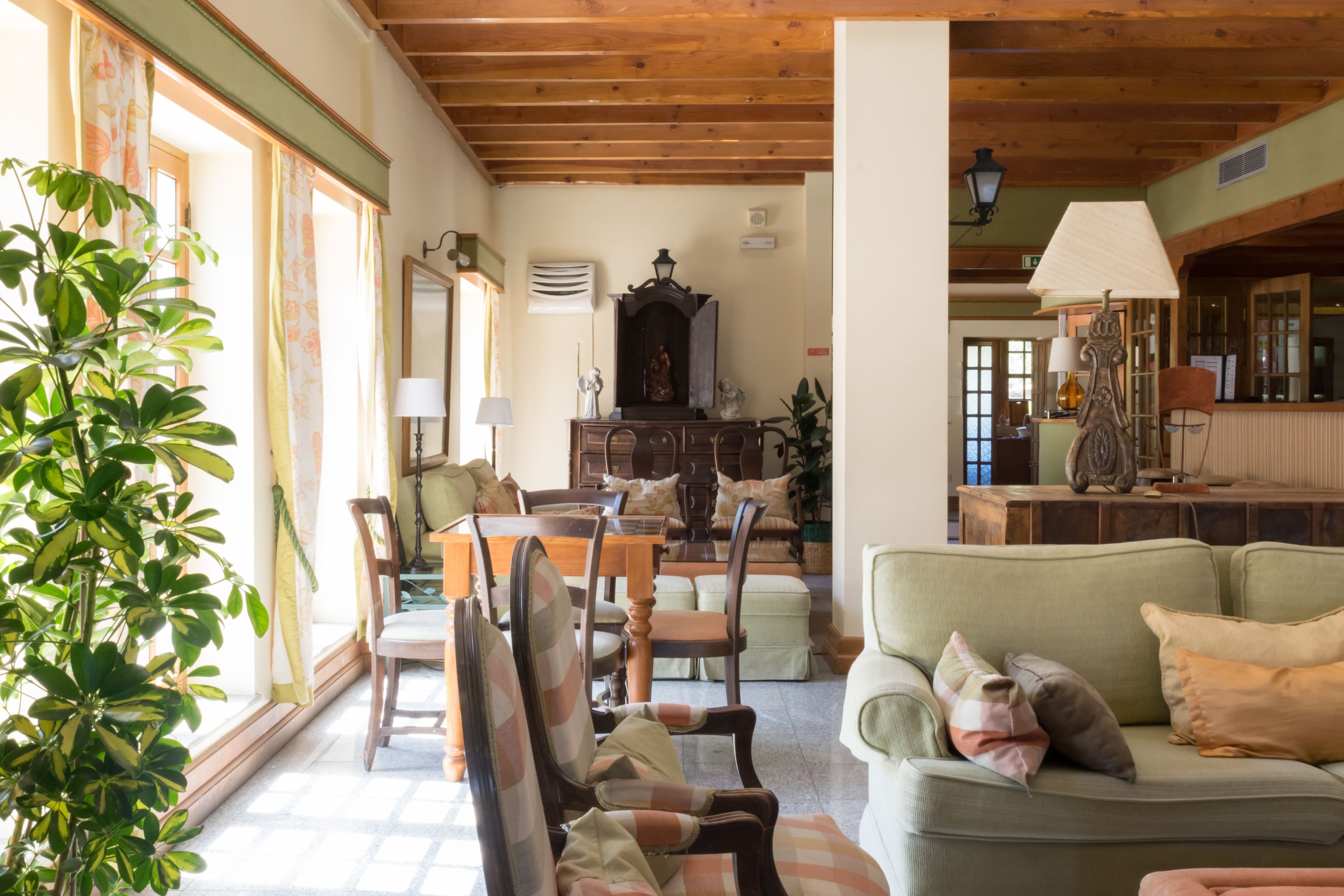 A cozy living room with a wooden ceiling, a dining area with chairs and a table, and a green sofa with cushions.