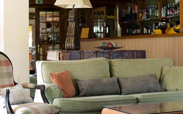 Una sala de estar acogedora con un sofá verde, un sillón estampado y una lámpara.
