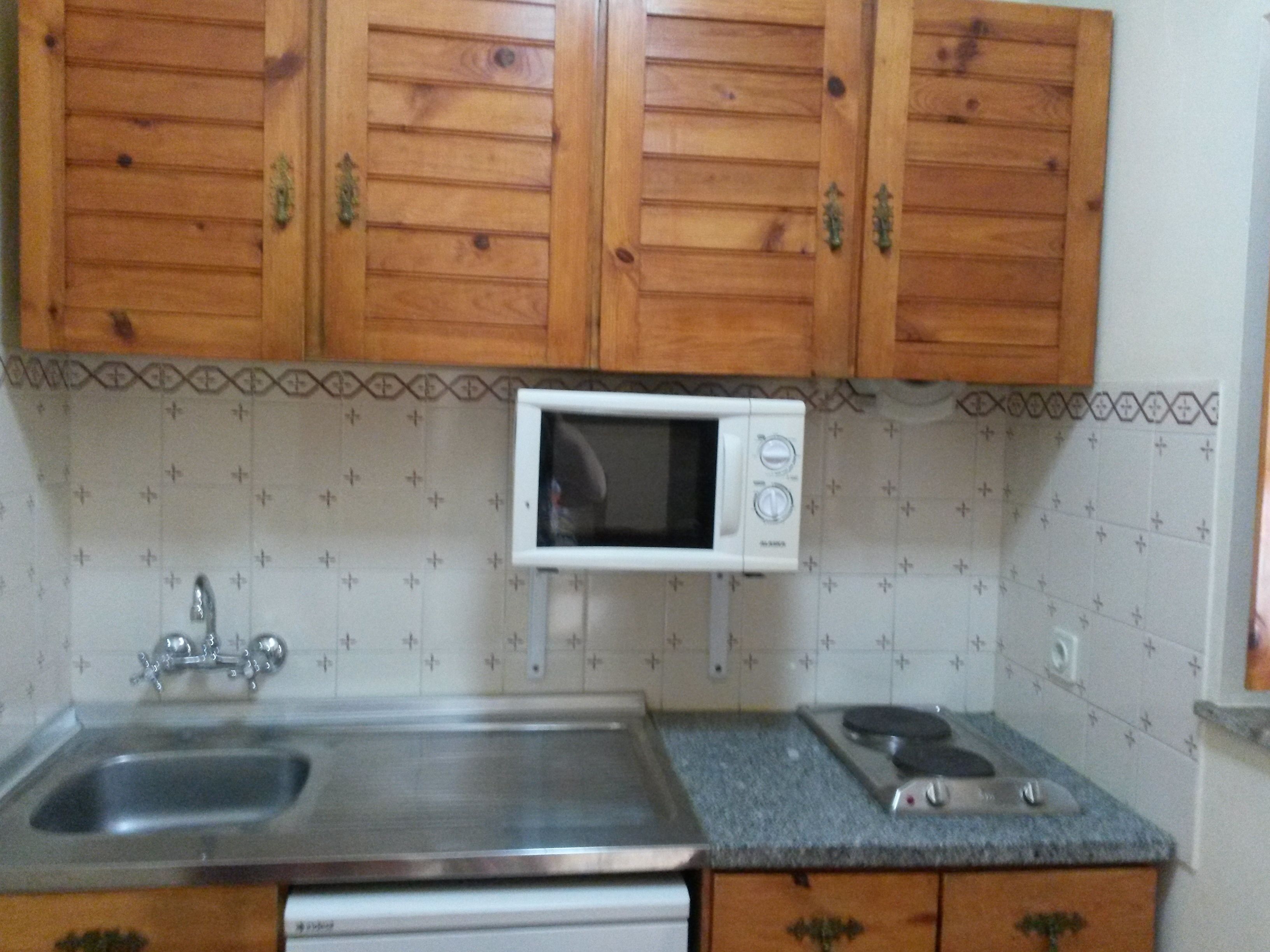 A kitchen with wooden cabinets, a white microwave, a stainless steel sink, and a gas stove.