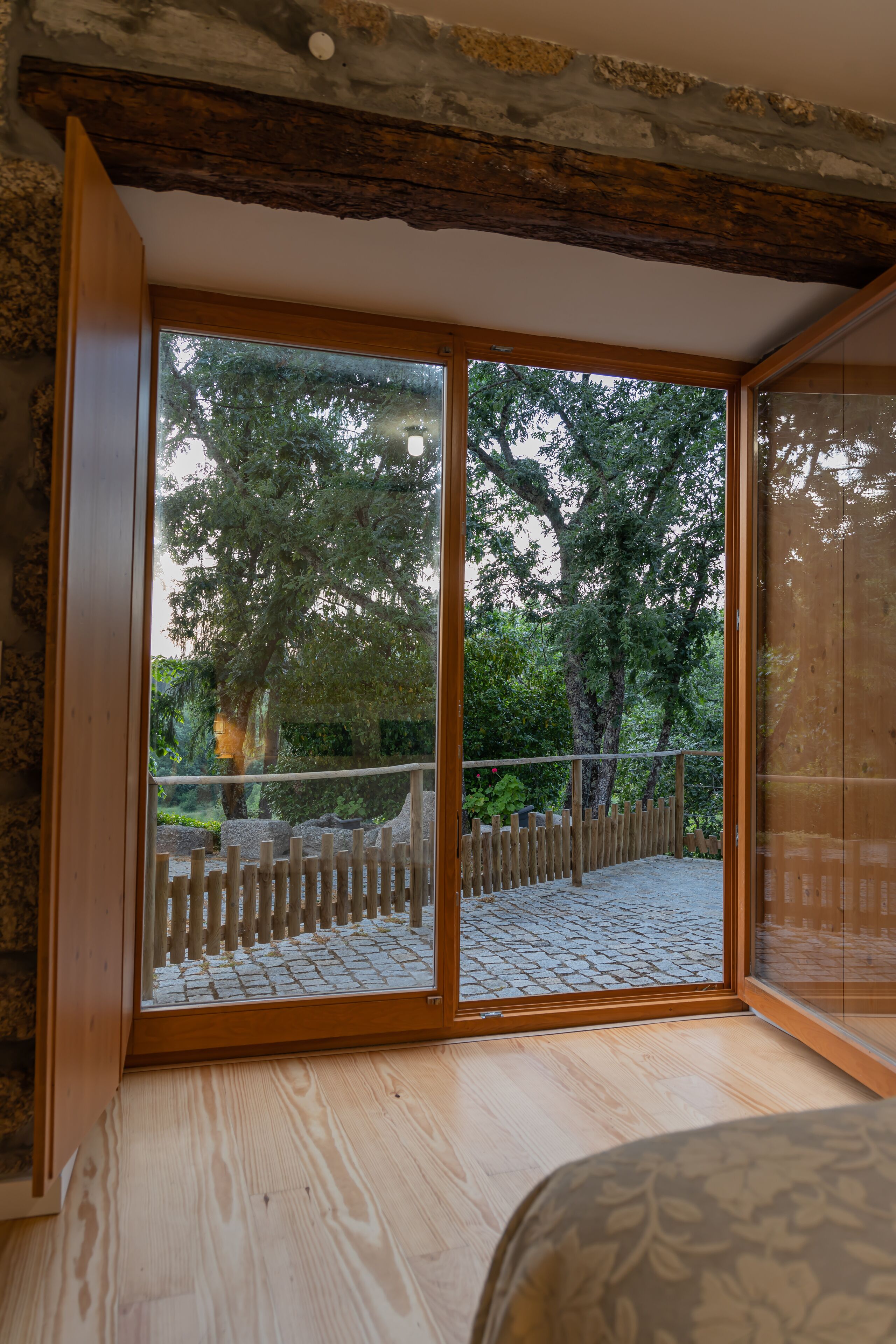 Una habitación con un amplio ventanal corredera que da a un espacio exterior con terraza de madera y un camino de piedra.