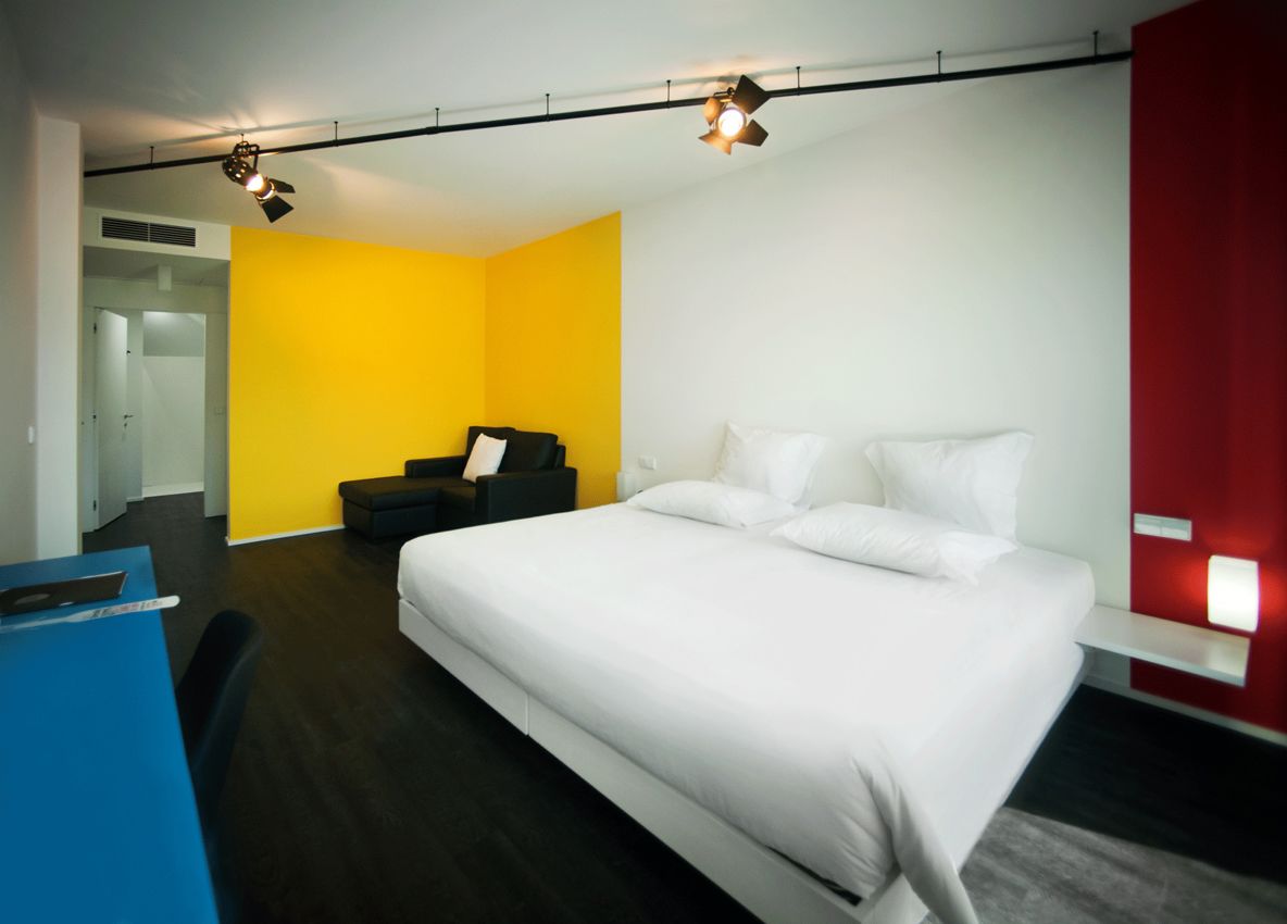 A modern hotel room with a large bed, a desk, and a bright yellow accent wall.