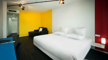 A modern hotel room with a large bed, a desk, and a bright yellow accent wall.