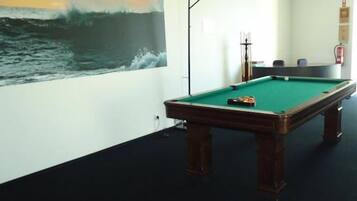 A billiards table in a room with a large painting of a wave on the wall.