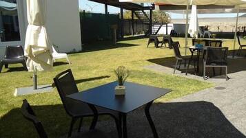 Un área de patio al aire libre con mesa y sillas, una planta pequeña en maceta y sombrillas que proporcionan sombra.