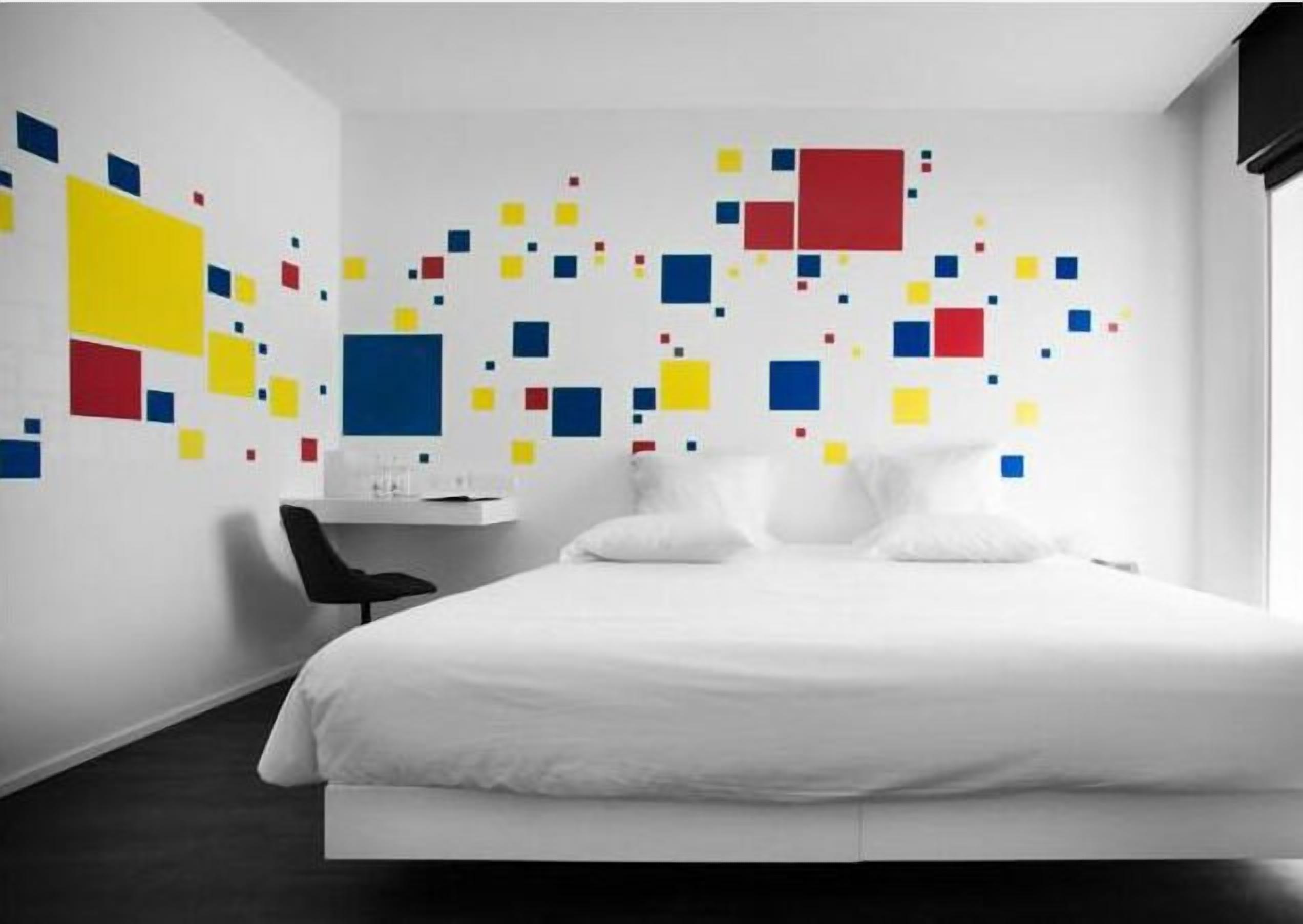 Quarto de hotel moderno com uma cama branca, uma escrivaninha e uma cadeira.