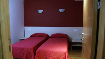 A room with two single beds, each with a red bedspread, and a wooden headboard.