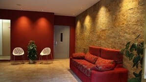 Un moderno vestíbulo con un sofá rojo, dos sillas blancas y una pared de piedra texturizada.