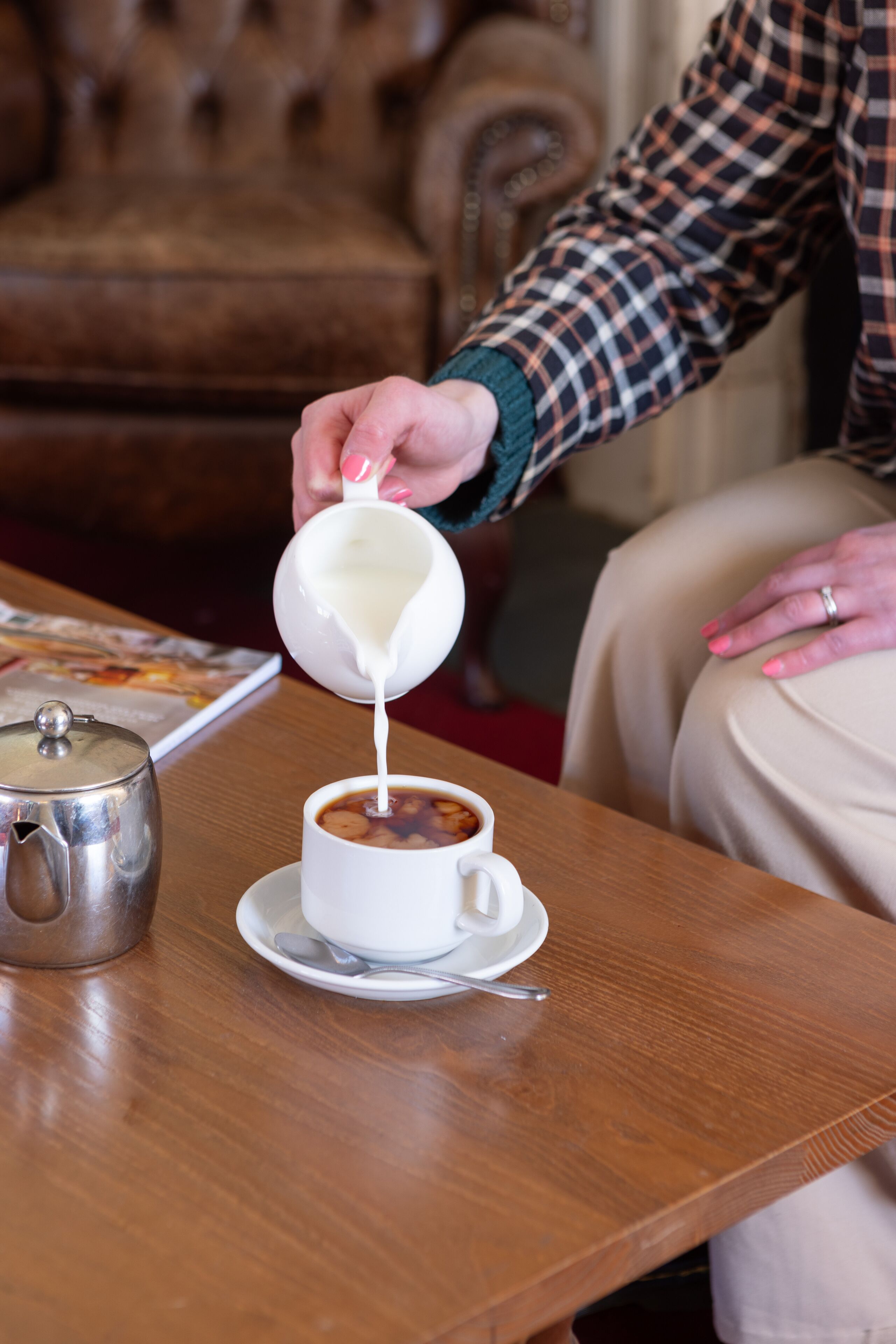 Alguém está a verter leite para uma chávena de café sobre uma mesa de madeira.