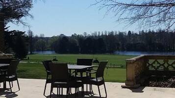 An outdoor patio with a table and chairs, a stone bench, and a view of a lake and trees.