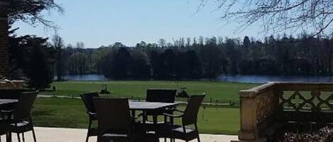 Un patio al aire libre con una mesa y sillas, un banco de piedra y vistas a un lago y árboles.