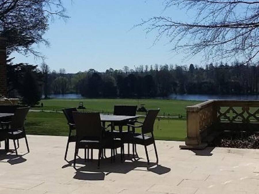 Eine Terrasse im Freien mit Tisch und Stühlen, einer Steinbank und Blick auf einen See und Bäume.