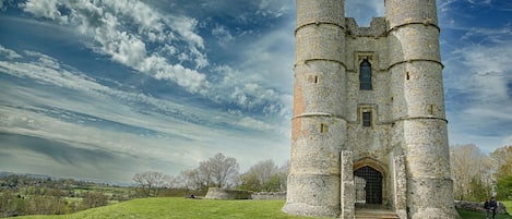 A historic stone tower with a central arched entrance and two cylindrical towers, set on a grassy hill with a clear sky.