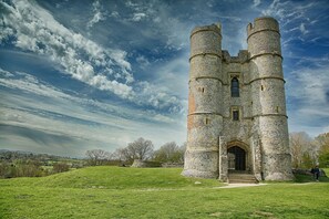 A historic stone tower with a central arched entrance and two cylindrical towers, set on a grassy hill with a clear sky. - Donnington Grove Country Club (Newbury)