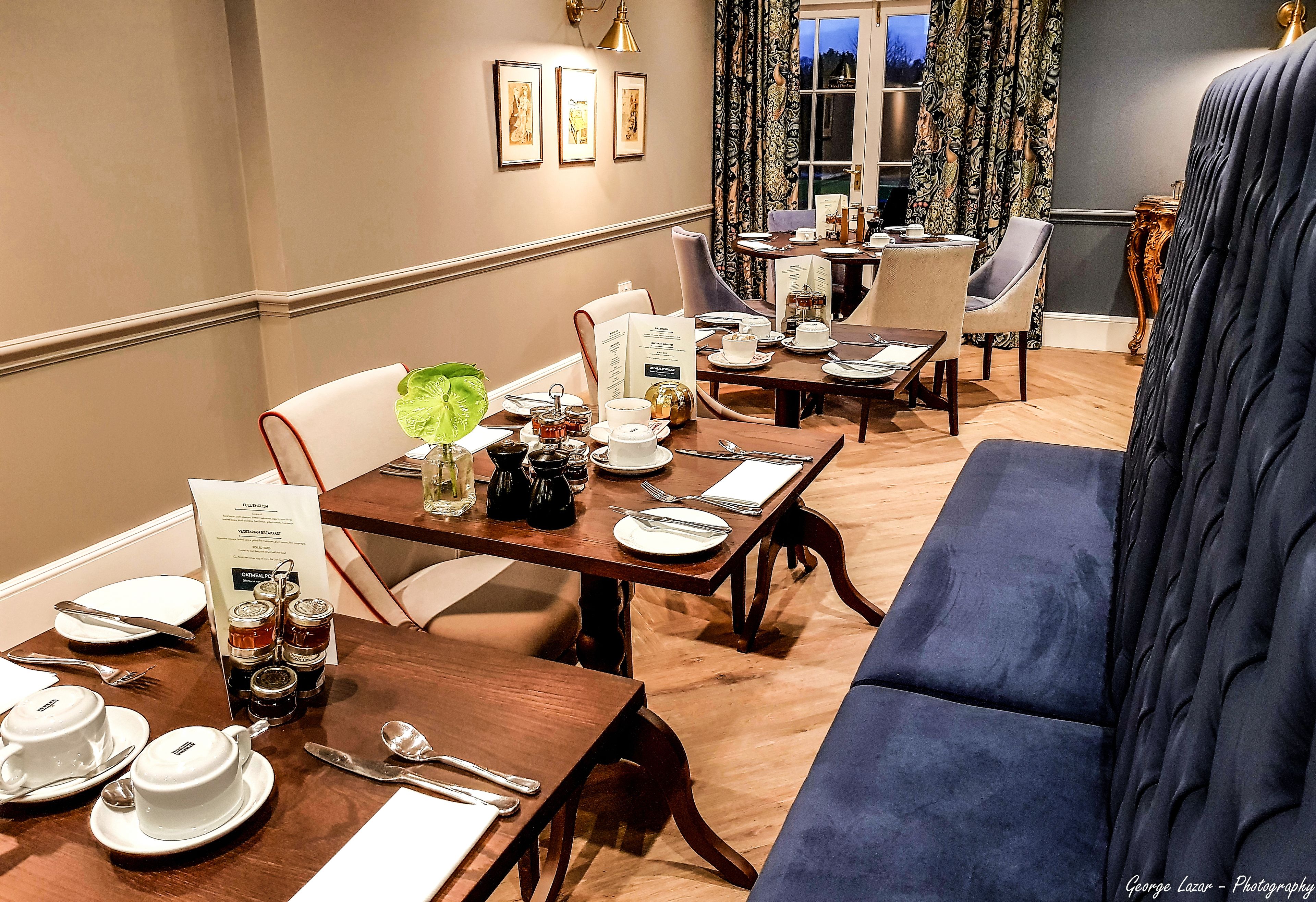A dining area with tables set for service, a sofa, and a view of the outdoors.