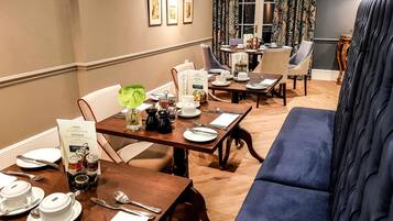 A dining area with tables set for service, a sofa, and a view of the outdoors.