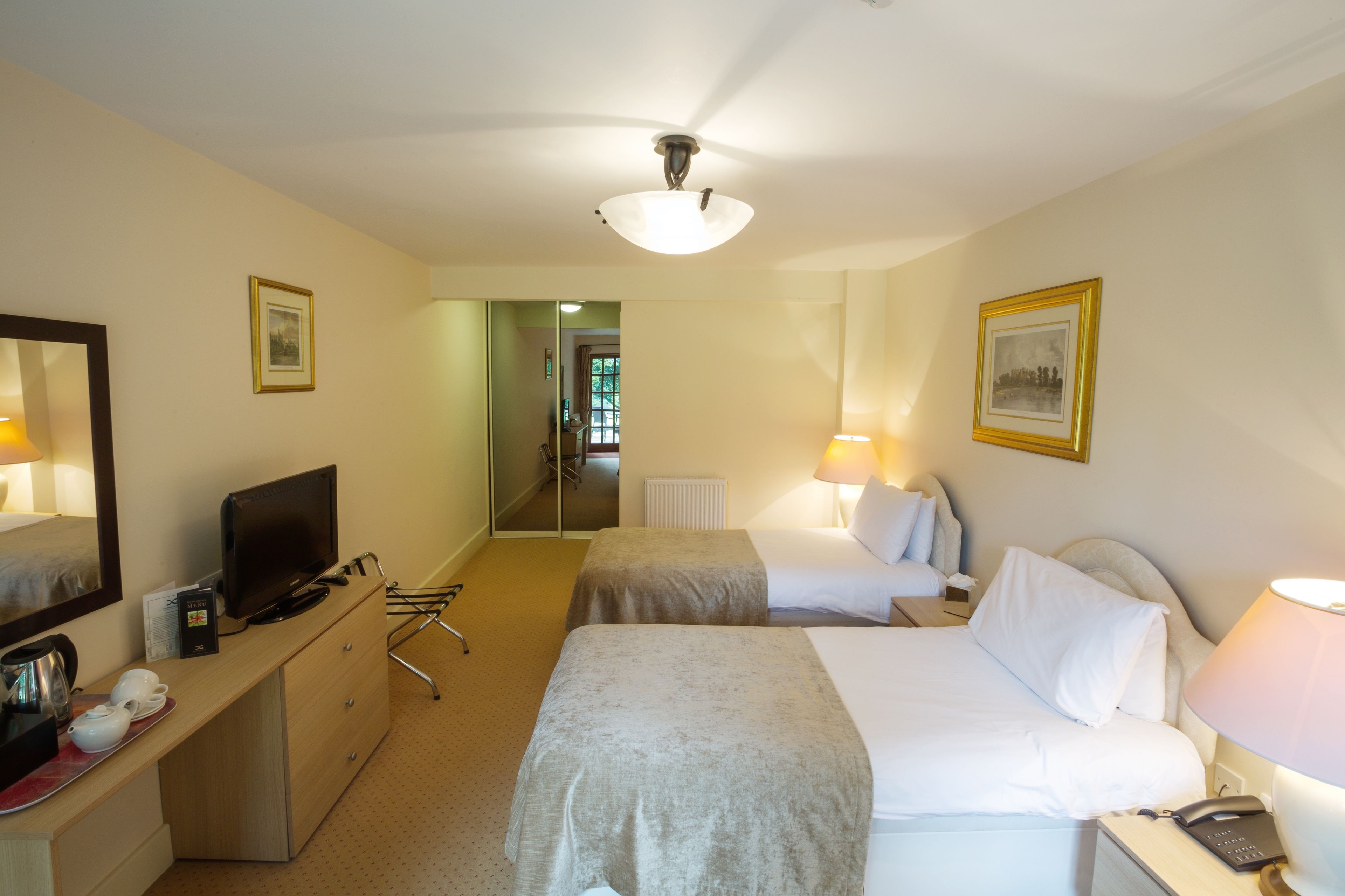 A hotel room with two beds, a desk with a television, a lamp, and a mirror.