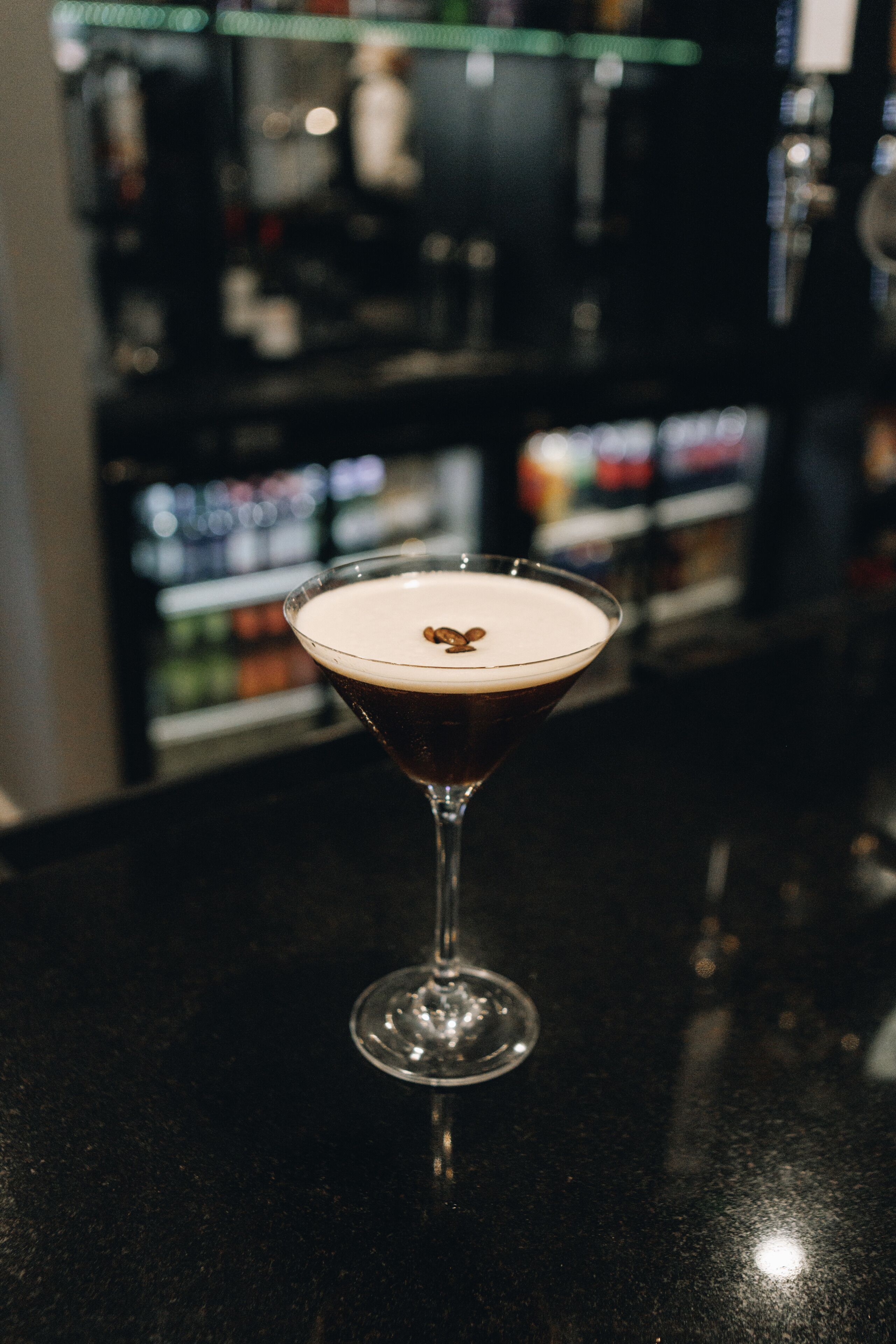 A martini glass with a frothy top on a bar counter.